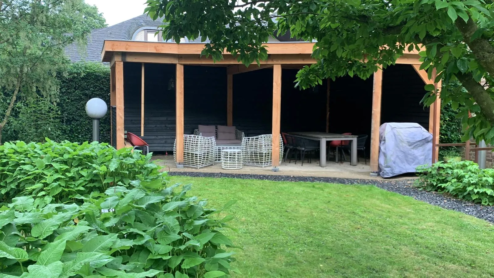 Houten overkapping met loungeset en eettafel in de tuin